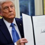 Donald Trump holding the tariff executive order, a large document bearing his signature