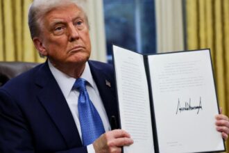 Donald Trump holding the tariff executive order, a large document bearing his signature