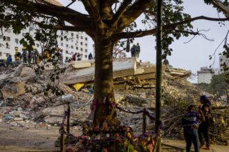 A completely destroyed building being searched by several people looking for survivors and the deceased
