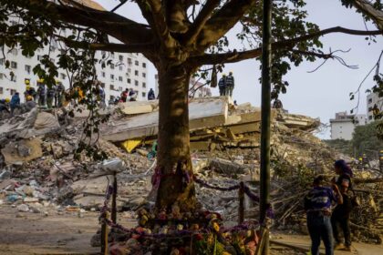 A completely destroyed building being searched by several people looking for survivors and the deceased