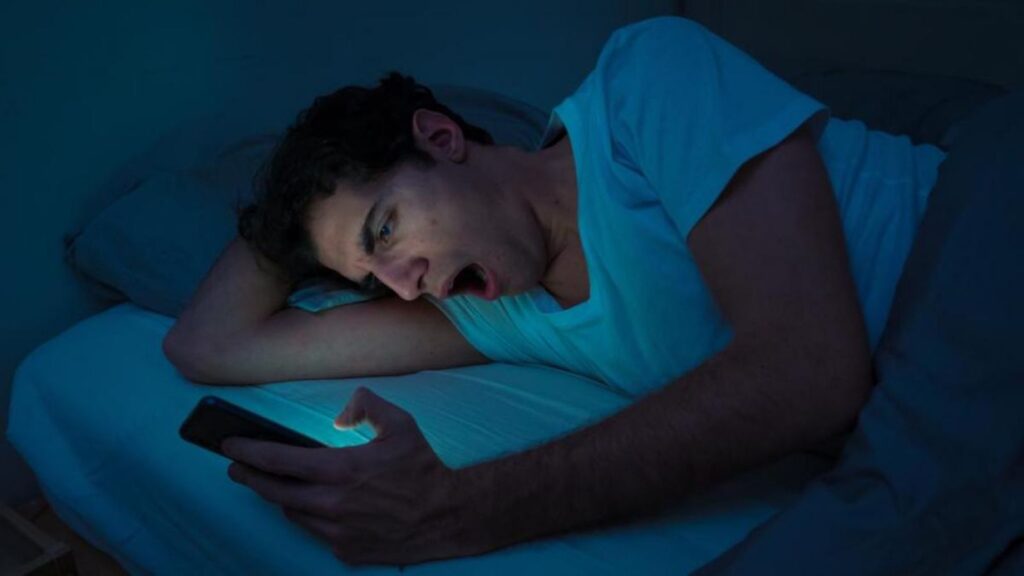 A young man holding and looking at his cellphone in a completely dark room