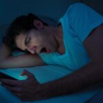 A young man holding and looking at his cellphone in a completely dark room