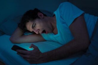 Do You wake up to use the bathroom? These habits before bed could be the reason A young man holding and looking at his cellphone in a completely dark room