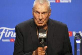 Don Nelson sitting in front of several microphones and speaking to everyone in attendance