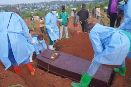 Several doctors burying multiple Ebola victims in a large field spanning many acres