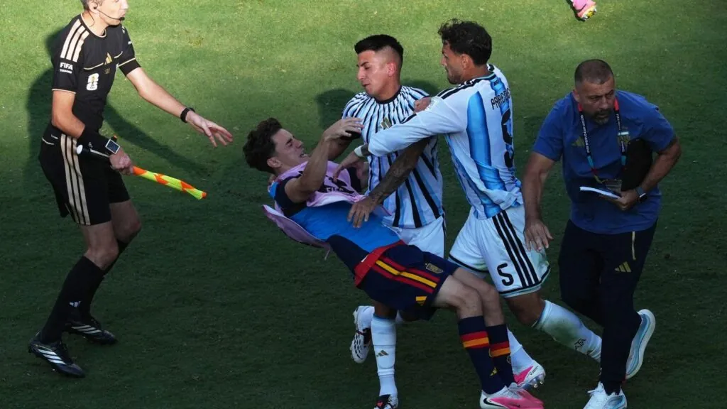 An Argentine player forcefully pushing a Spanish player, knocking him to the ground