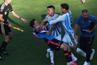 An Argentine player forcefully pushing a Spanish player, knocking him to the ground
