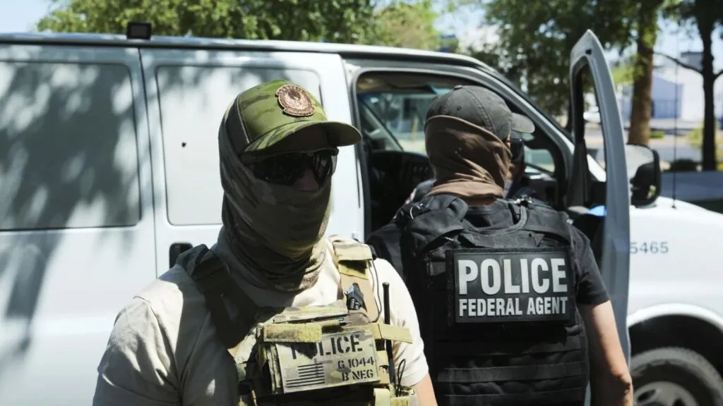 Two uniformed ICE agents wearing vests and face masks to avoid being recognized