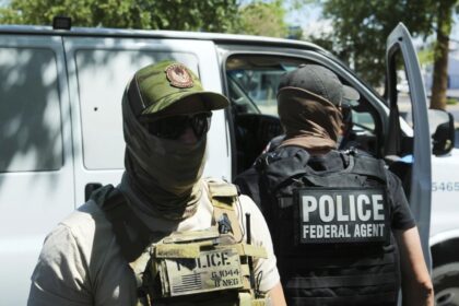 Two uniformed ICE agents wearing vests and face masks to avoid being recognized