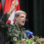 General Hatami speaking into a microphone decorated with flowers while wearing an Iranian military uniform