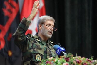 General Hatami speaking into a microphone decorated with flowers while wearing an Iranian military uniform
