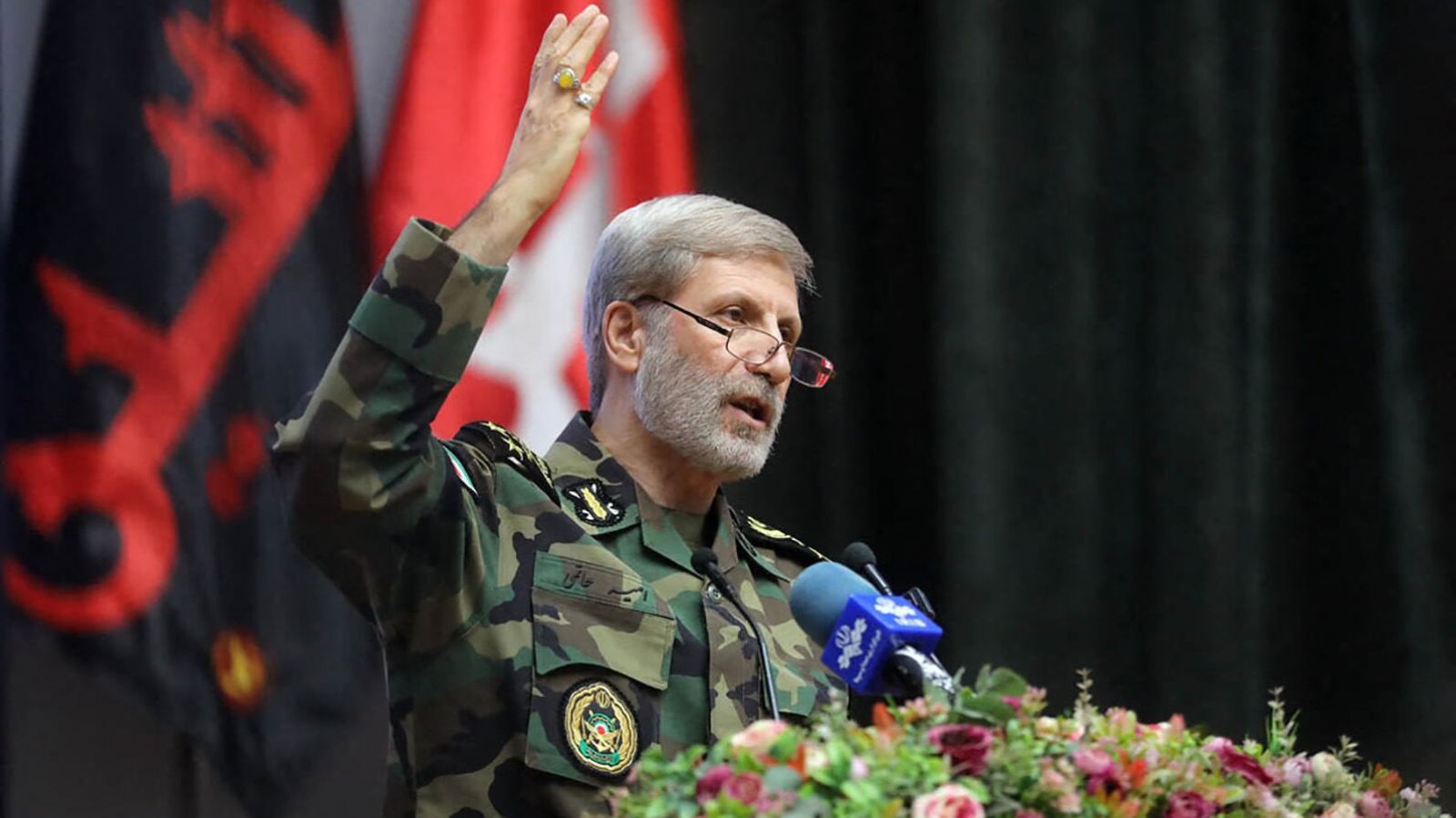 General Hatami speaking into a microphone decorated with flowers while wearing an Iranian military uniform