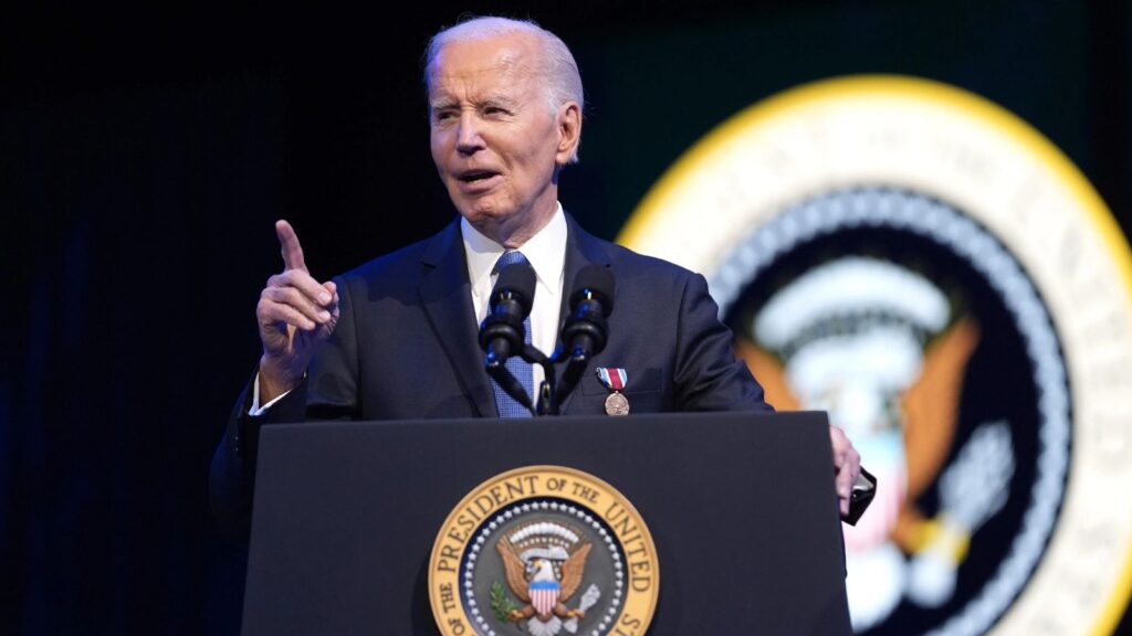 Biden wearing a handsome, elegant suit while speaking at a podium in front of many prominent people from the United States