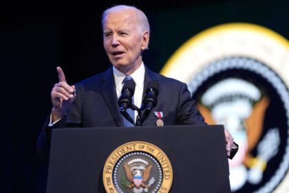 Biden wearing a handsome, elegant suit while speaking at a podium in front of many prominent people from the United States