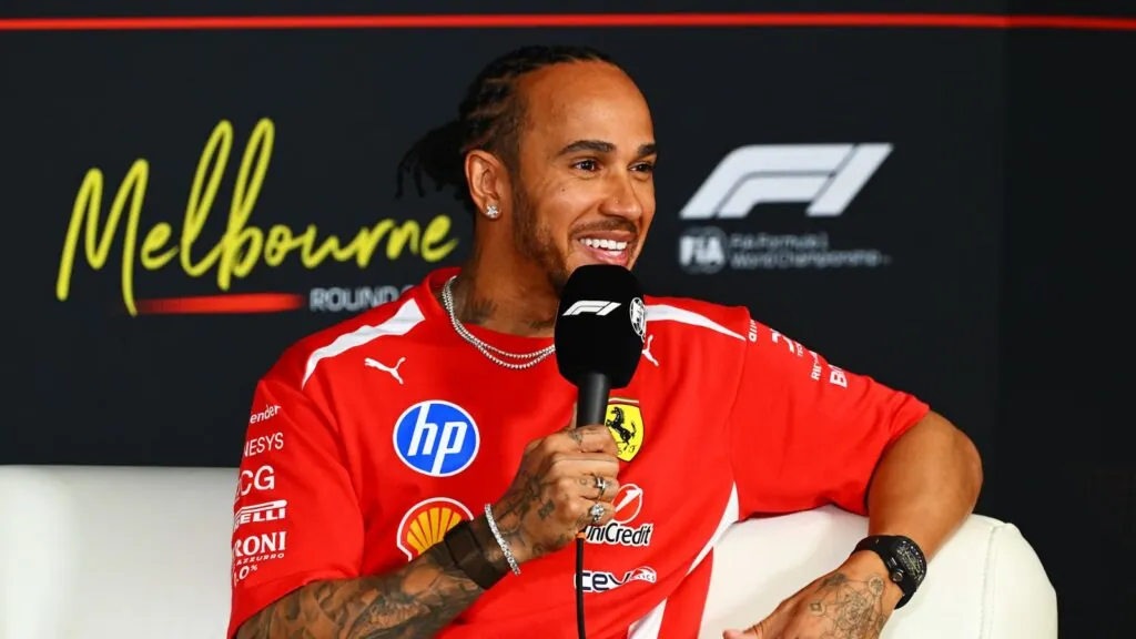Hamilton sitting in a chair while being interviewed in his Ferrari uniform