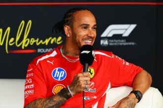 Hamilton sitting in a chair while being interviewed in his Ferrari uniform
