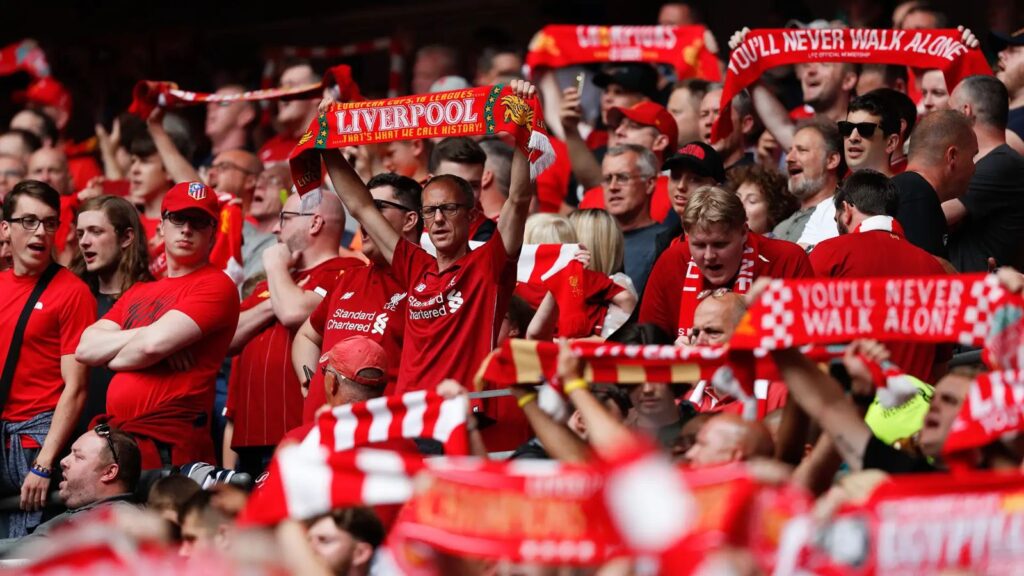 Many Liverpool fans at Anfield raising scarves and flags supporting their favorite team