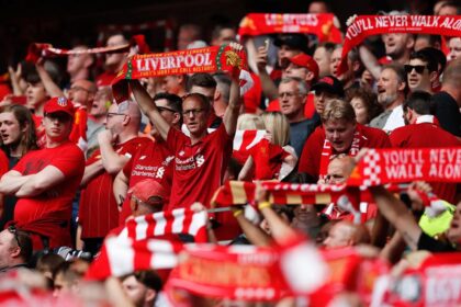Many Liverpool fans at Anfield raising scarves and flags supporting their favorite team