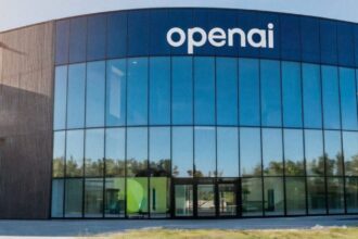 A panoramic view of OpenAI's headquarters featuring a modern glass façade with numerous windows and the company name displayed prominently in white on the building