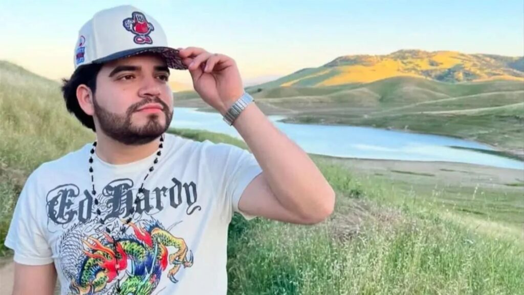 The influencer taking a photo of himself in a scenic landscape with mountains and a lake behind him