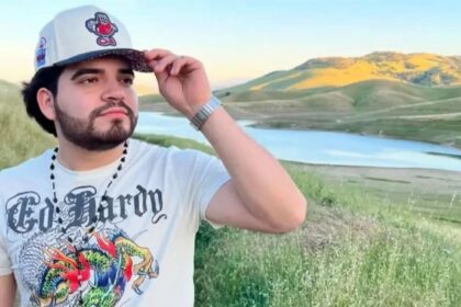 The influencer taking a photo of himself in a scenic landscape with mountains and a lake behind him