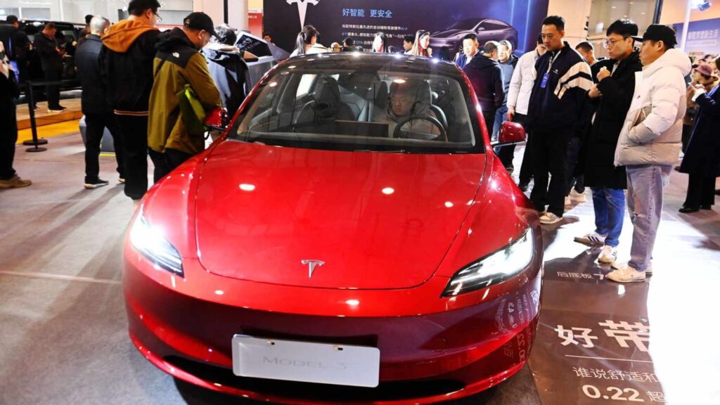 A red Tesla being test-driven by a man at an auto show