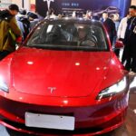 A red Tesla being test-driven by a man at an auto show