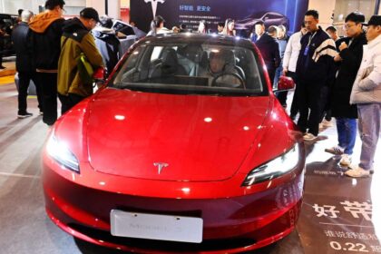 A red Tesla being test-driven by a man at an auto show