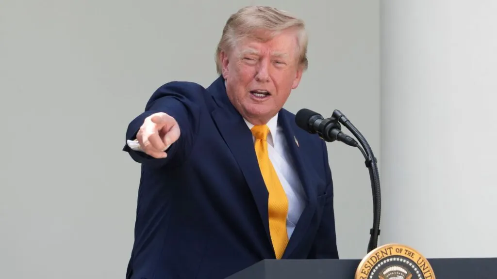 Trump pointing at someone in the audience while speaking into a microphone with a happy expression