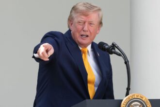 Trump pointing at someone in the audience while speaking into a microphone with a happy expression