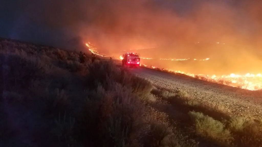 A pickup truck driving through a path with intense fire after the wildfire