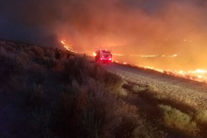 A pickup truck driving through a path with intense fire after the wildfire