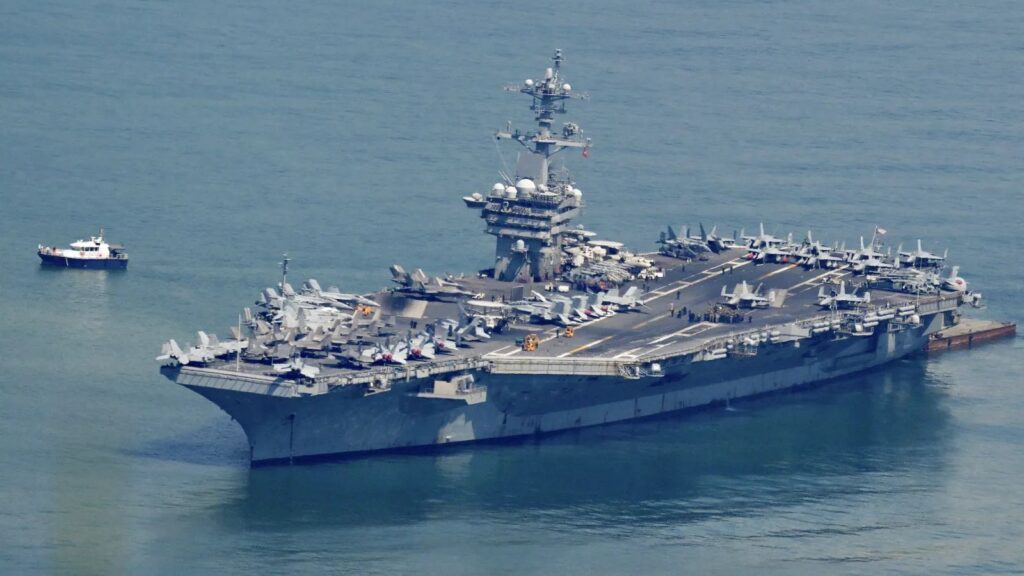 The imposing and massive aircraft carrier sailing in open waters, accompanied by a small vessel alongside it