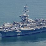 The imposing and massive aircraft carrier sailing in open waters, accompanied by a small vessel alongside it