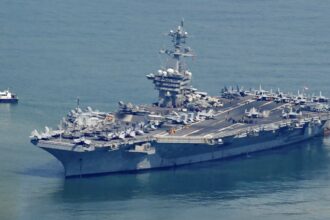 The imposing and massive aircraft carrier sailing in open waters, accompanied by a small vessel alongside it