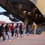 "A large airplane receiving several deported individuals to transport them back to their home country