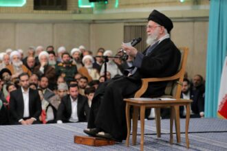The leader of the Iranian regime sitting in a chair while surrounded by his followers