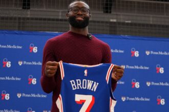 Jaylen Brown holding the Philadelphia jersey with the number 7 he will wear with the team