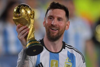 The Argentine star holding the World Cup trophy with one hand while smiling and showing it to the crowd