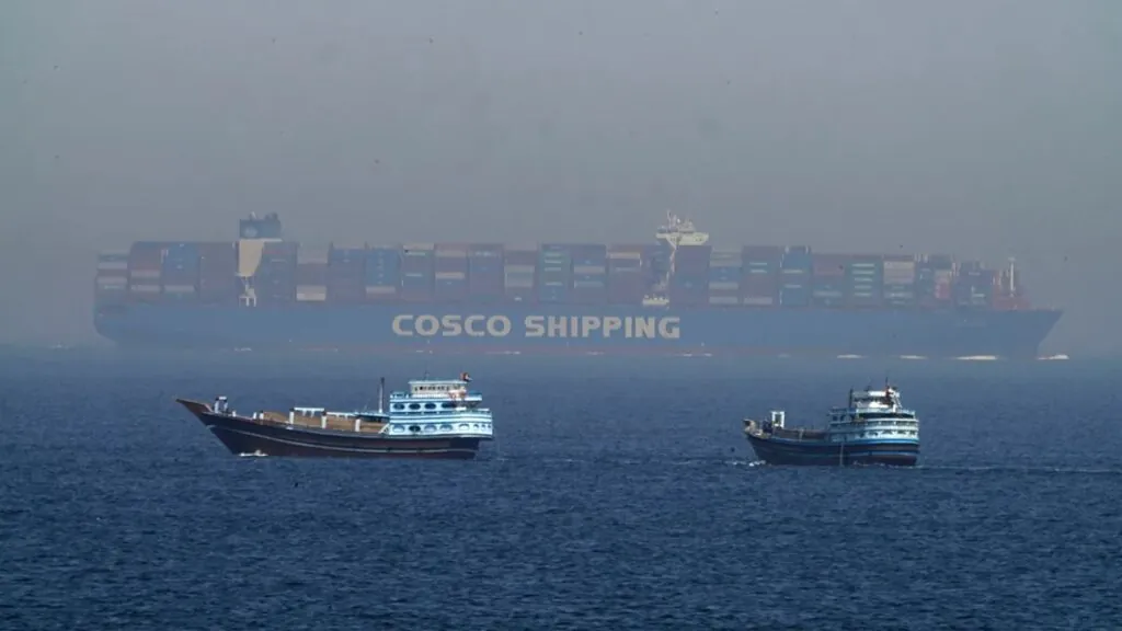 Several small boats at sea with a gigantic container ship behind them