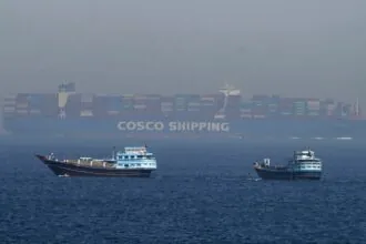 Several small boats at sea with a gigantic container ship behind them
