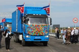 Russia and North Korea open historic first road bridge between the two countries Several blue trucks decorated with many flowers crossing the new bridge